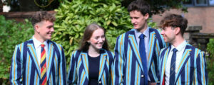 Four students in blue striped blazers walk together outdoors, smiling and talking.