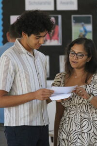 Two adults, a young man in a striped shirt and a woman with glasses, review papers together.